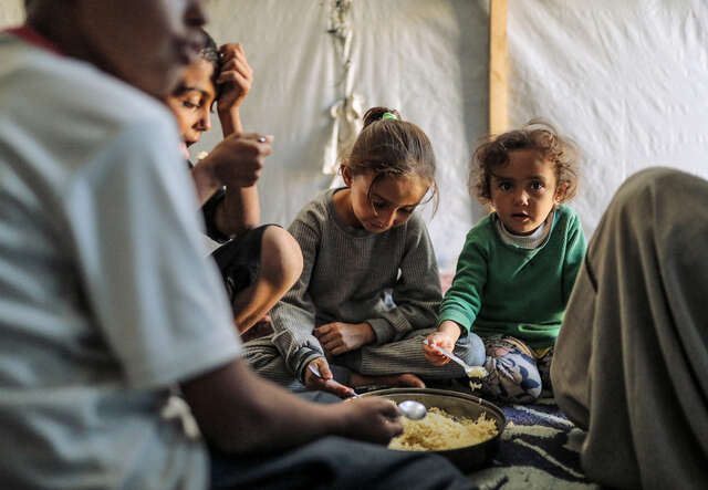 En familj i Gaza sitter i sitt tält och äter mat.